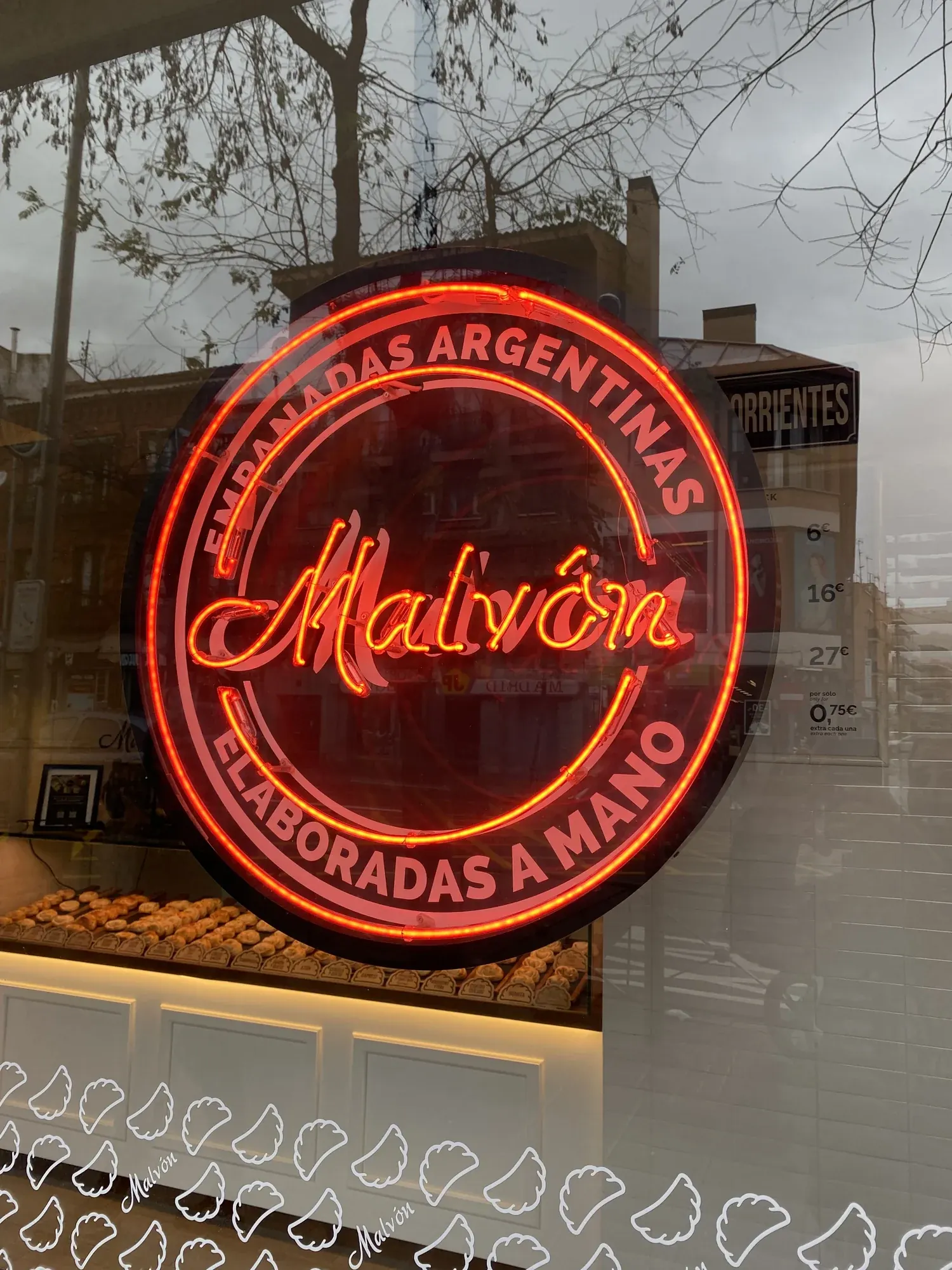 Rótulo circular de neón rojo de Empanadas Malvón encendido en el escaparate