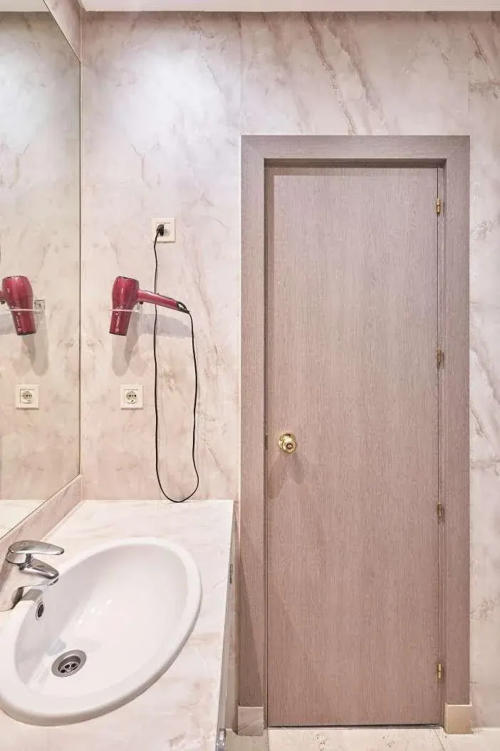 Baño de hotel con encimera y paramentos revestidos en efecto mármol
