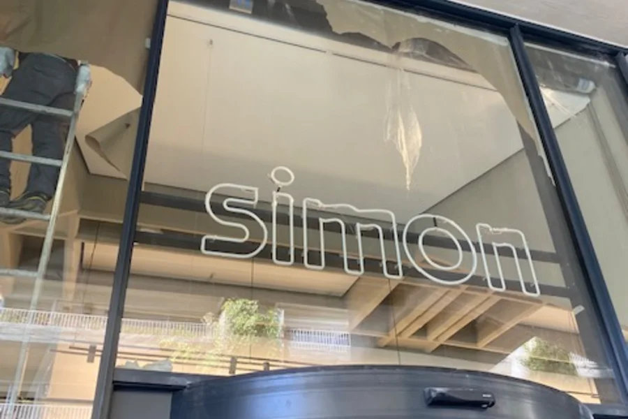 Rótulo de neón de Simon apagado sobre la fachada acristalada, con el local todavía en obra